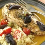 Chicken marbella on a dinner plate and topped with dried prunes, olives, and capers.