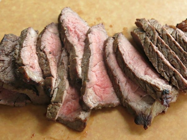 Slices of best London Broil recipe cut across the grain on cutting board.