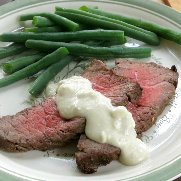London Broil topped with Blue Cheese Sauce on plate next to green beans.