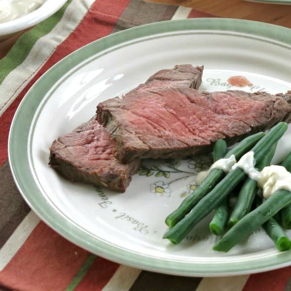 2 slices of medium rare London Broil on plate next to green beans.