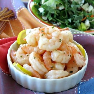 Skillet shrimp piled in a bowl with salad and pasta in the background.