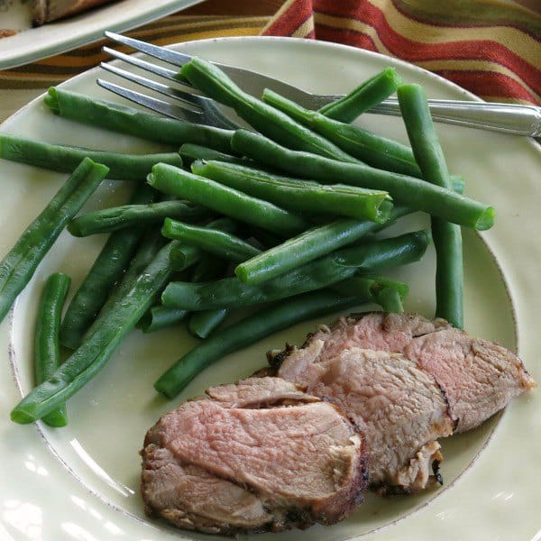 3 slices of red wine pork tenderloin on a plate with green beans.