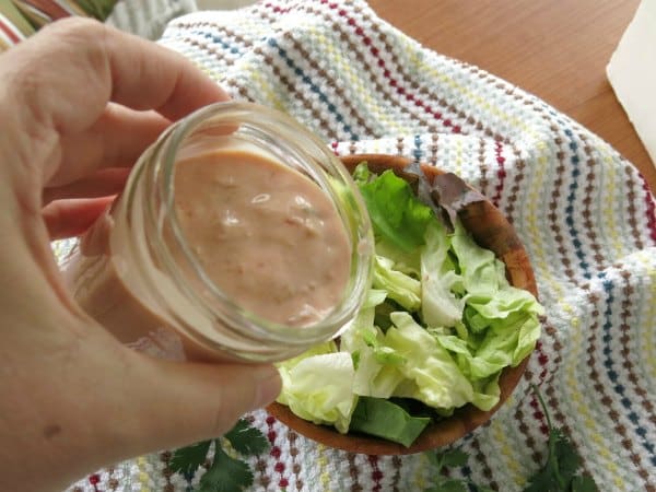 Hand pouring a jar with healthy taco salad dressing over lettuce