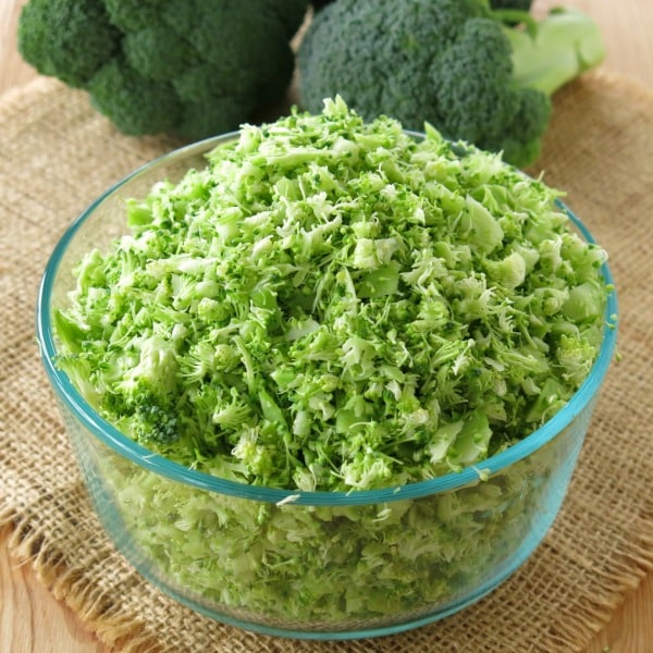 Bowl of riced broccoli with heads of broccoli behind it.