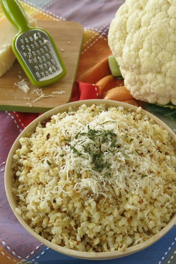 Arroz de coliflor asado con queso parmesano y una cabeza de coliflor al fondo