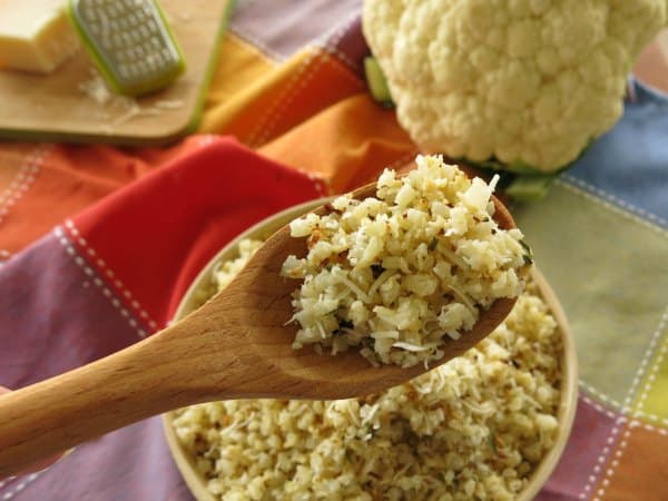 Arroz de coliflor con ajo y parmesano asado en una cuchara de madera sobre un bol.