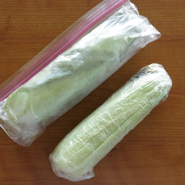 Two cobs of corn: one wrapped in plastic and the other in a plastic bag, ready to go into the freezer.