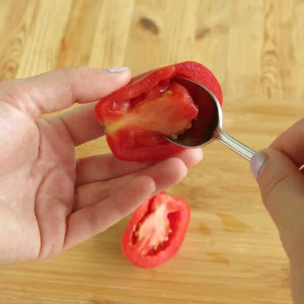 Spoon removing flesh from the center of half a Roma tomato