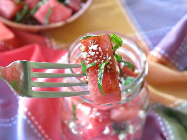 A chunk of watermelon salad with basil, feta and balsamic syrup on a fork.