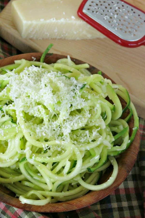 Garlic Parmesan Zucchini Noodles in serving bowl with Parmesan cheese and grater next to it.