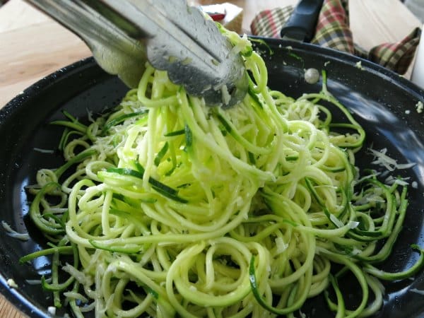 Tongs lifting Garlic Parmesan Zucchini Noodles out of skillet