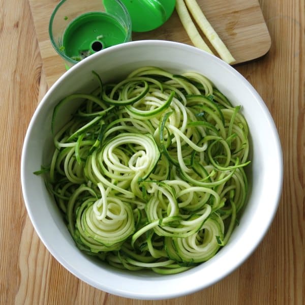 Spiralized zucchini noodles in a dish next to hand held spiralizer