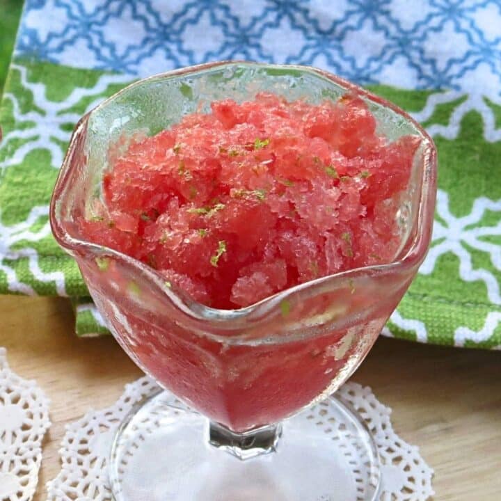 Watermelon Granita in a glass cup topped with lime zest and a colorful towel in the background.