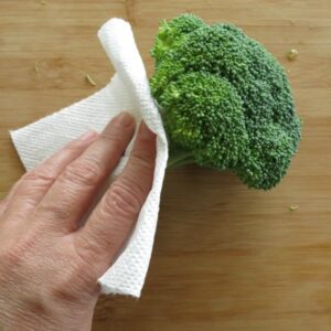 Hand drying stalk of broccoli with paper towel.