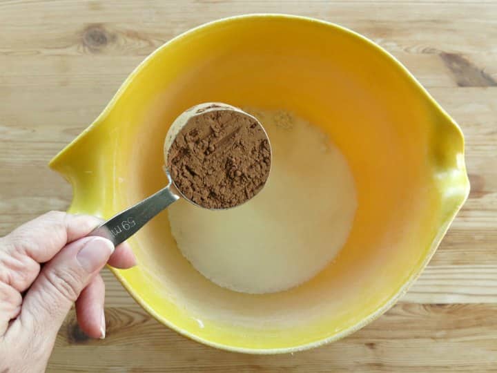 Measuring cup with cocoa powder being emptied into mixing bowl for chocolate pumpkin muffins