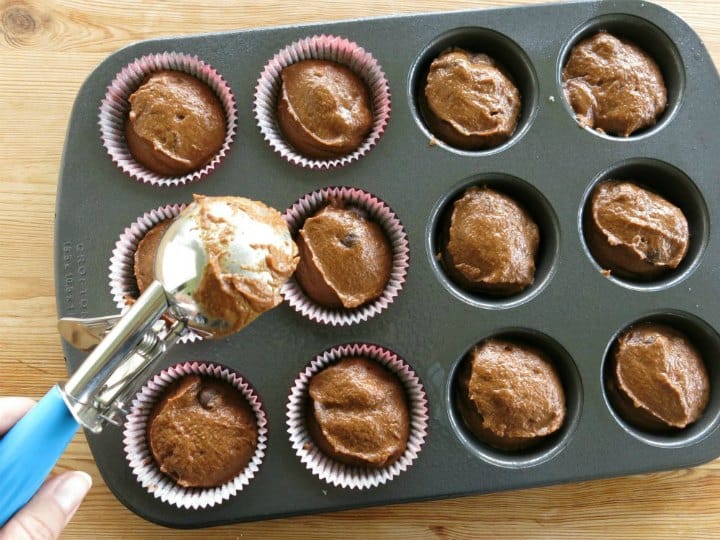 Ice cream scoop putting chocolate pumpkin muffin batter in cupcake baking pan.