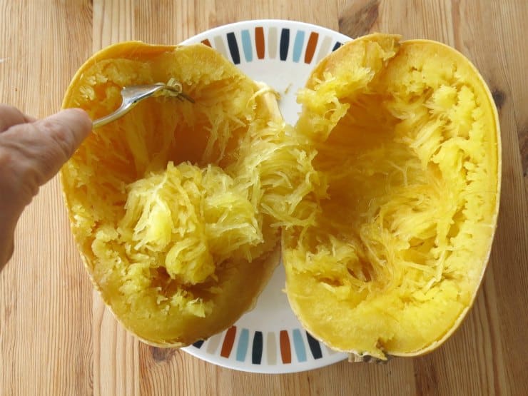 Fork removing spaghetti squash strands from gourd.