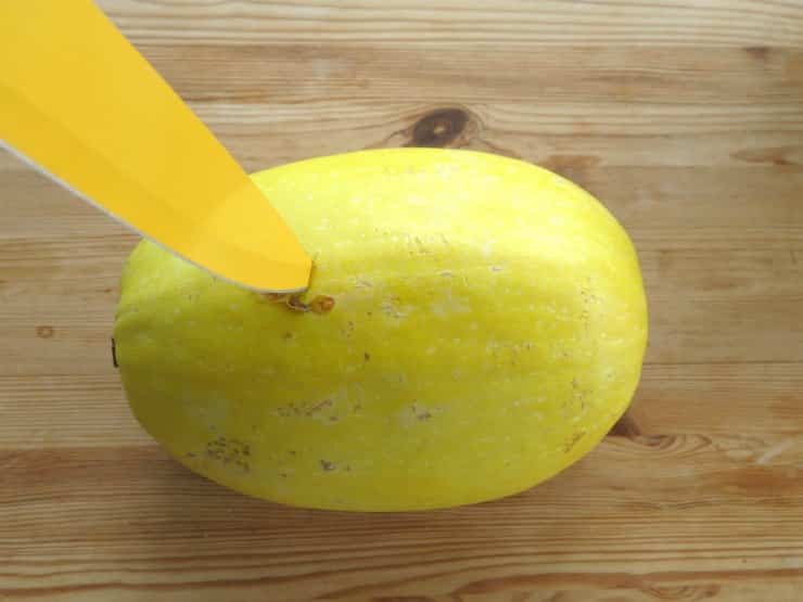 Tip of knife inserted in uncooked whole spaghetti squash.