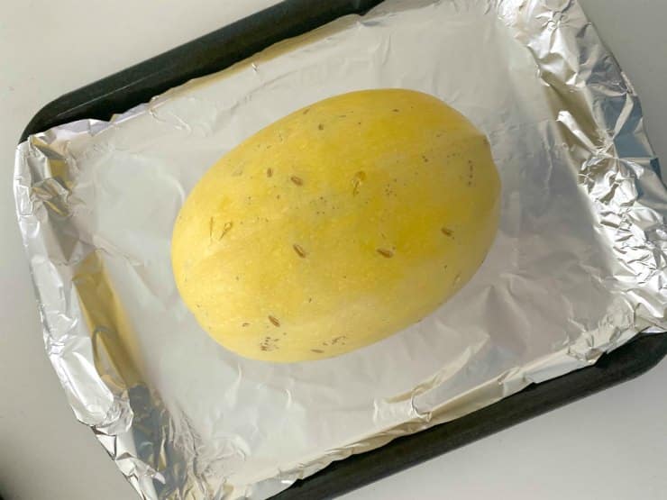 Spaghetti squash on baking sheet lined with aluminum foil.