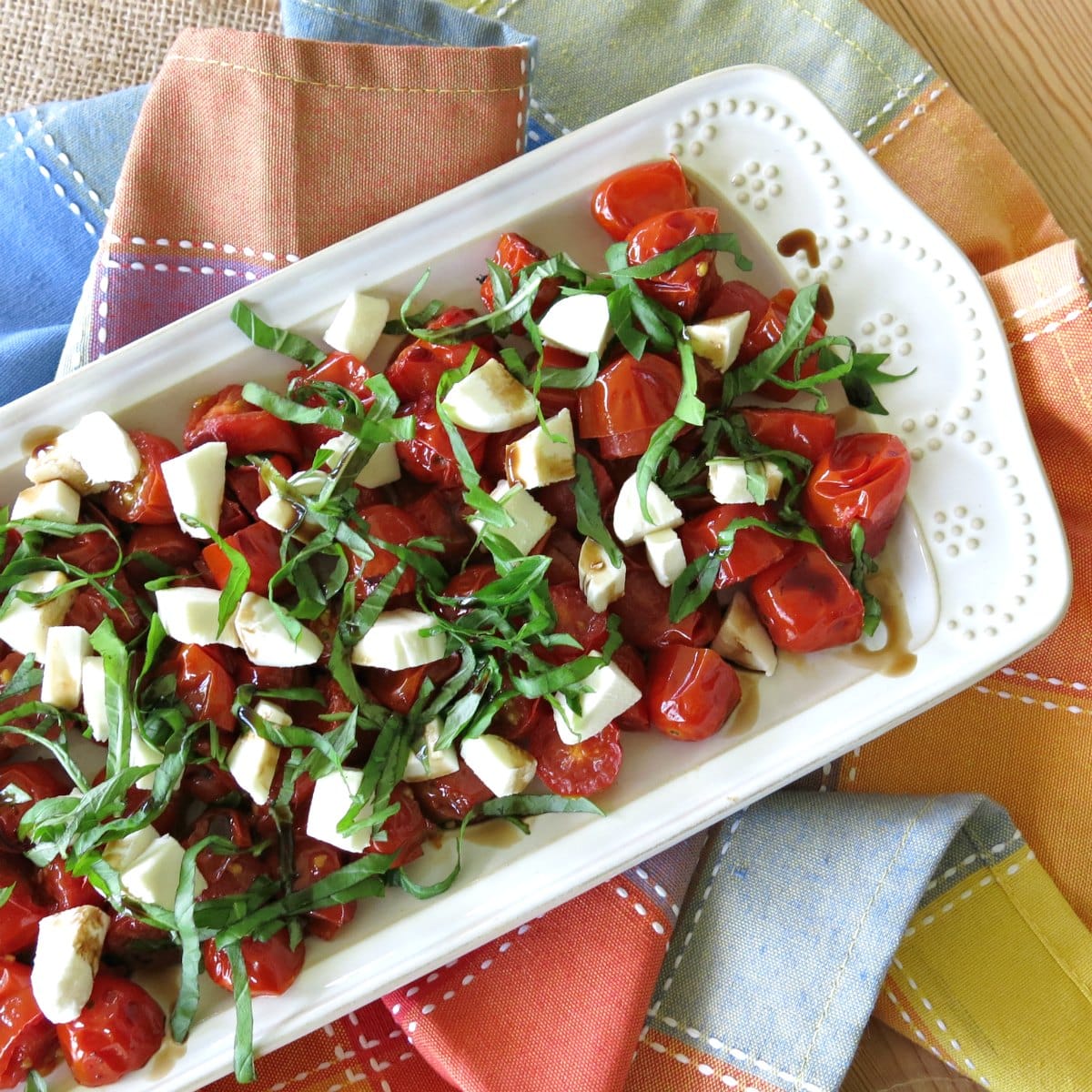 Roasted Grape Tomato Caprese Salad with mozzarella cheese, fresh basil, and balsamic glaze on a rectangular platter.