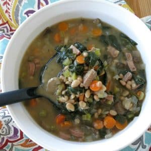 Ladle lifting white bean, sausage and spinach soup from bowl