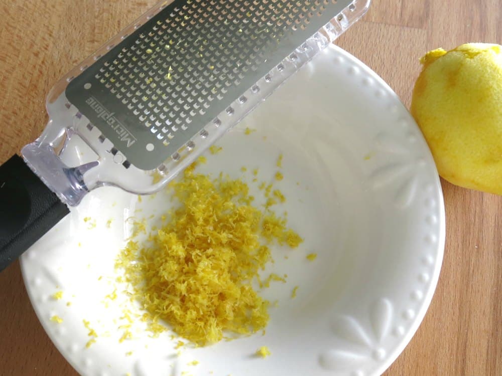 Lemon zest in bowl with microplane and zested lemon next to it