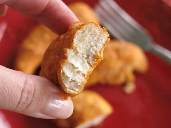 Hand holding Paprika Parmesan Chicken Nugget cooked in an air fryer with a bite removed to reveal white inside.