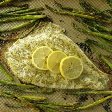 Cooked Turbot Fillet with mustard dill sauce and lemons on a baking sheet surrounded by asparagus