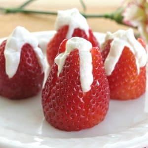 4 cheesecake stuffed strawberries on plate with flower behind it