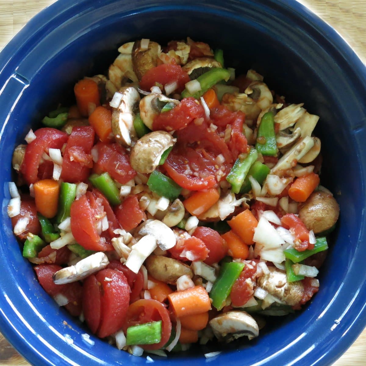 Slow cooker filled with vegetables, stewed tomatoes and chicken.