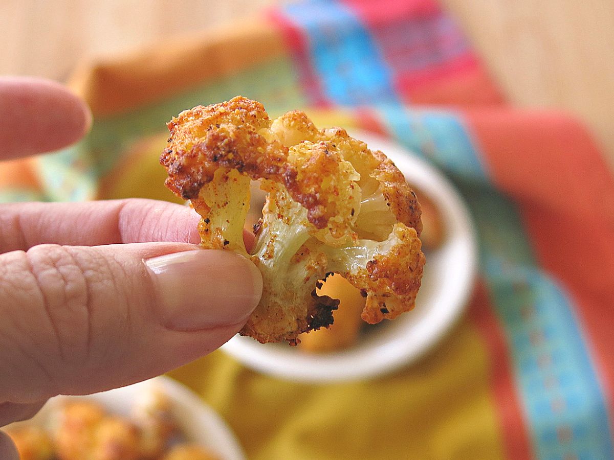 Fingers holding a Parmesan Cauliflower Bite over a bowl with more.