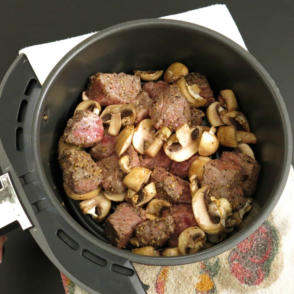 Partially cooked steak bites and mushrooms in air fryer basket.