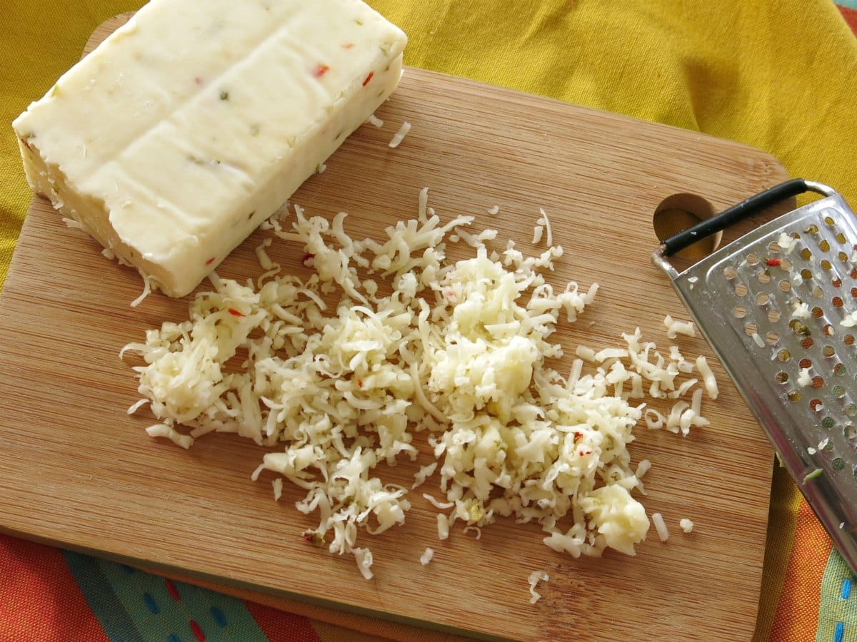 Block of Pepper Jack cheese on cutting board with shredded cheese and grater