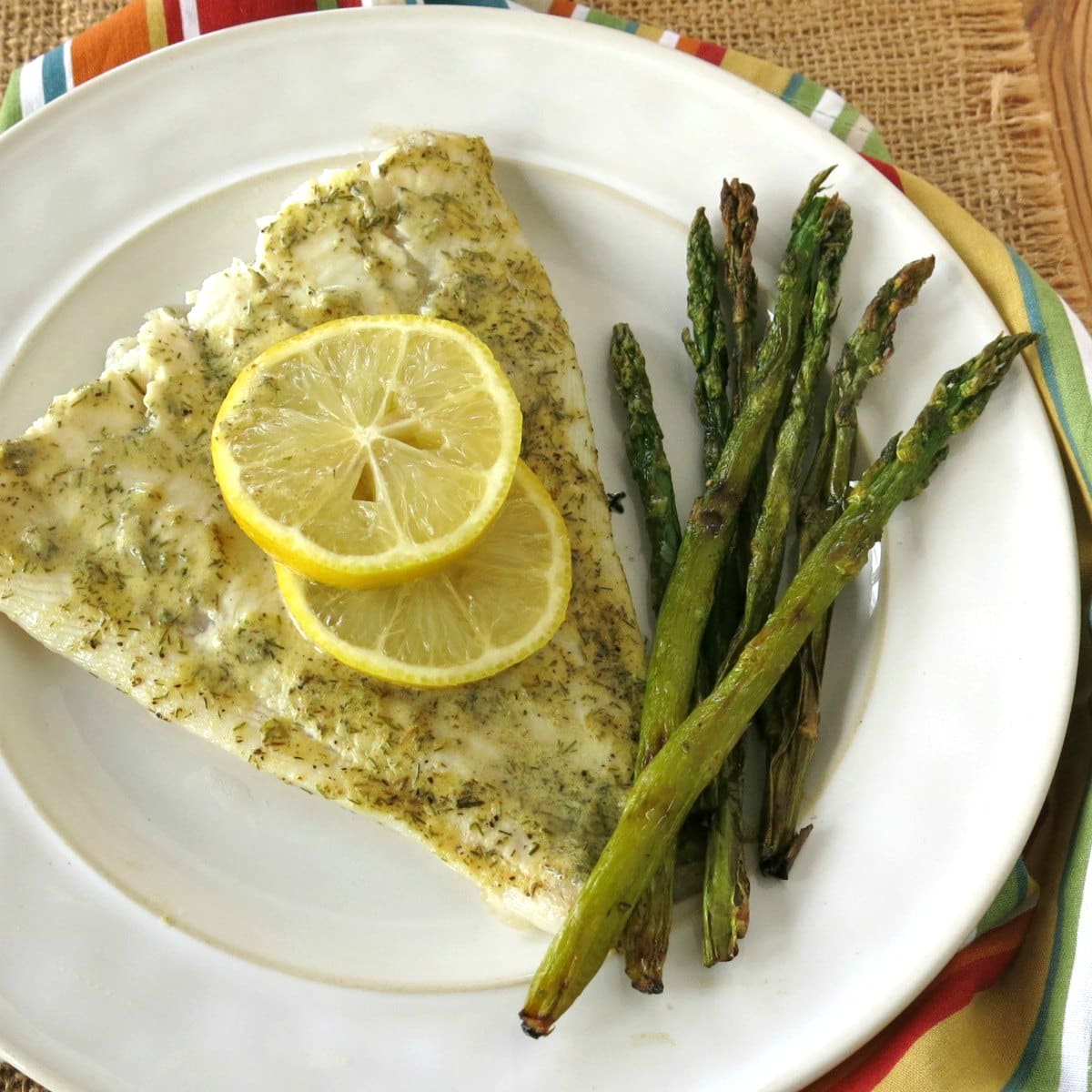 Serving of roasted Turbot with lemon slices on top and asparagus on plate.