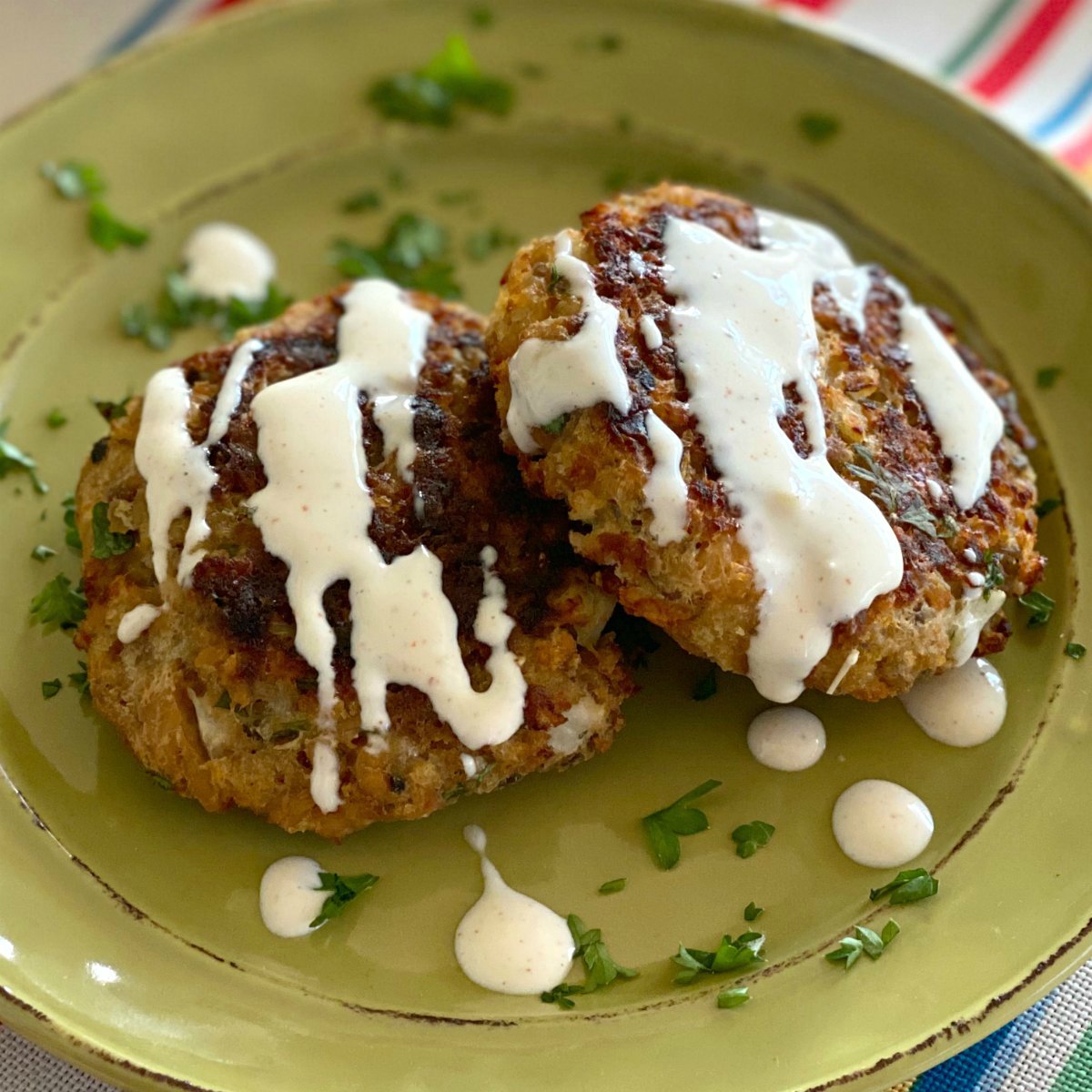 Two baked salmon cakes drizzled with aioli on a plate.