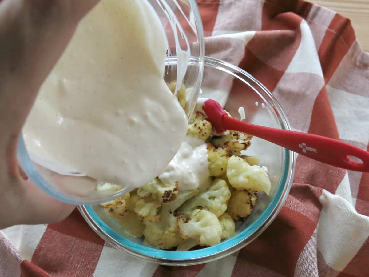 Crema sauce being poured over cauliflower in glass bowl