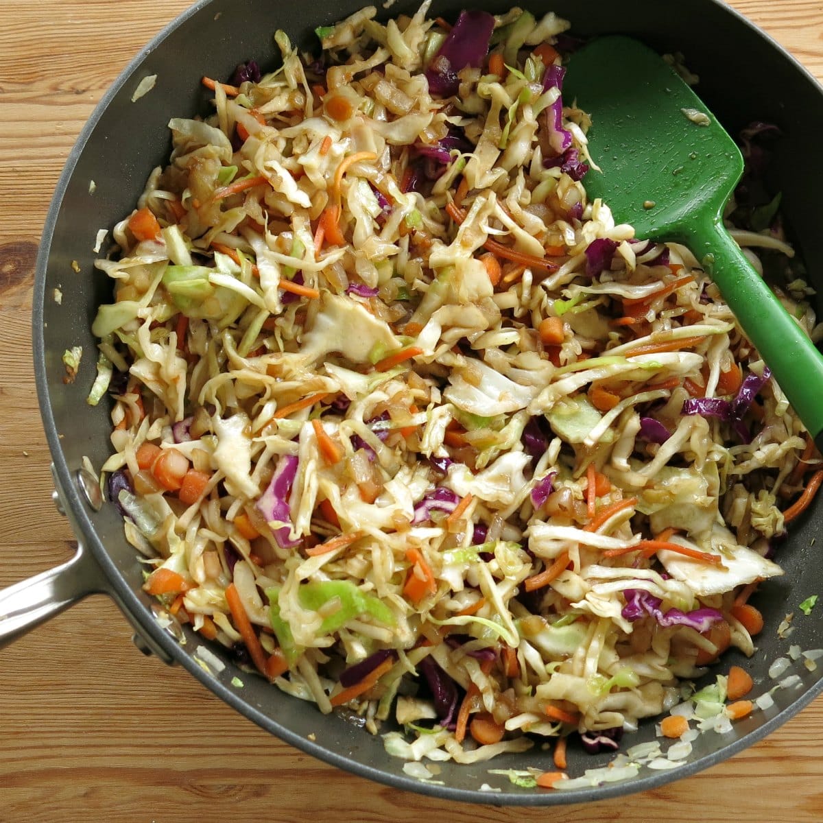 Skillet with cooked cooked cabbage, carrots, and spoon.