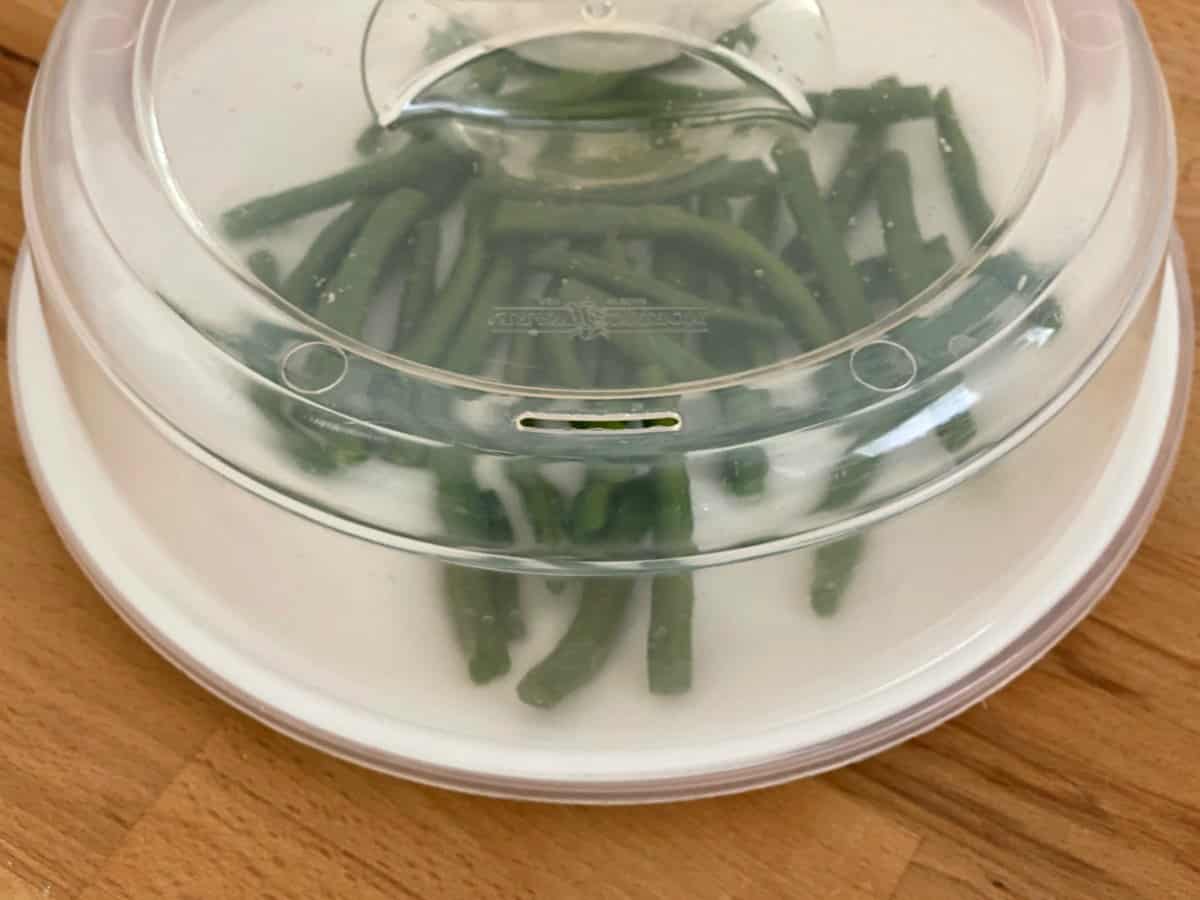 Green beans on plate covered with microwave lid cover.
