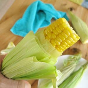 Hand holding microwave corn in husk being pulled out.