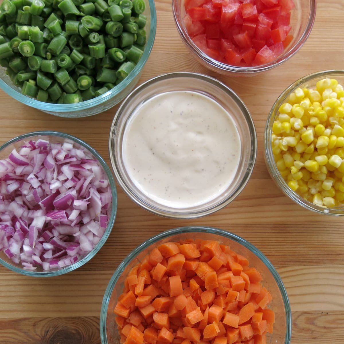 Small bowls with finely chopped vegetables surrounding a bowl of ranch dressing.