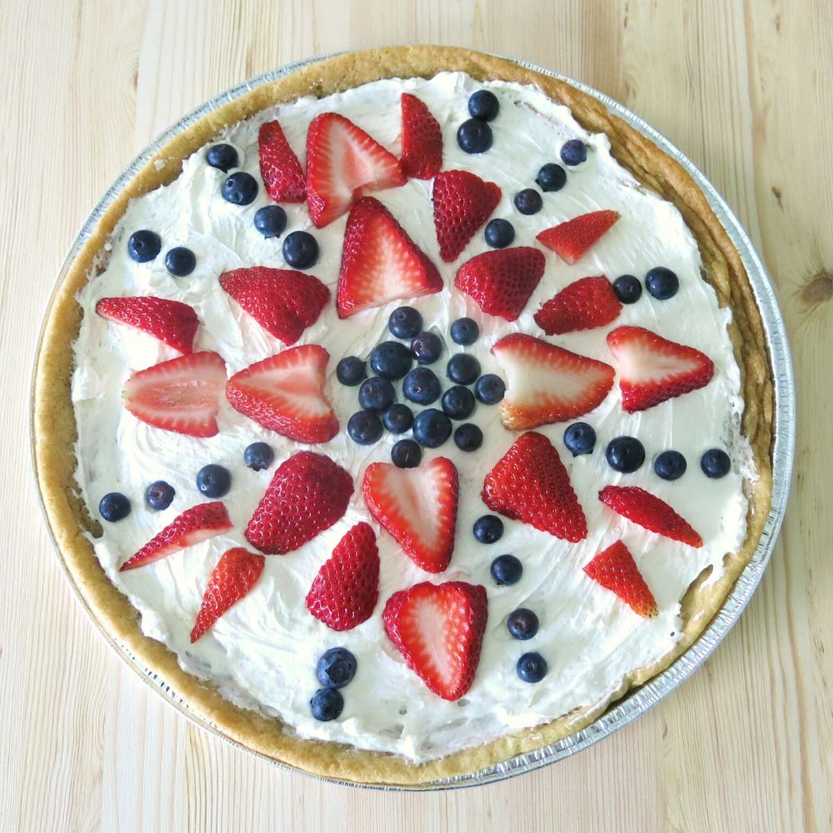 Fruit pizza cookie decorated with strawberries and blueberries.