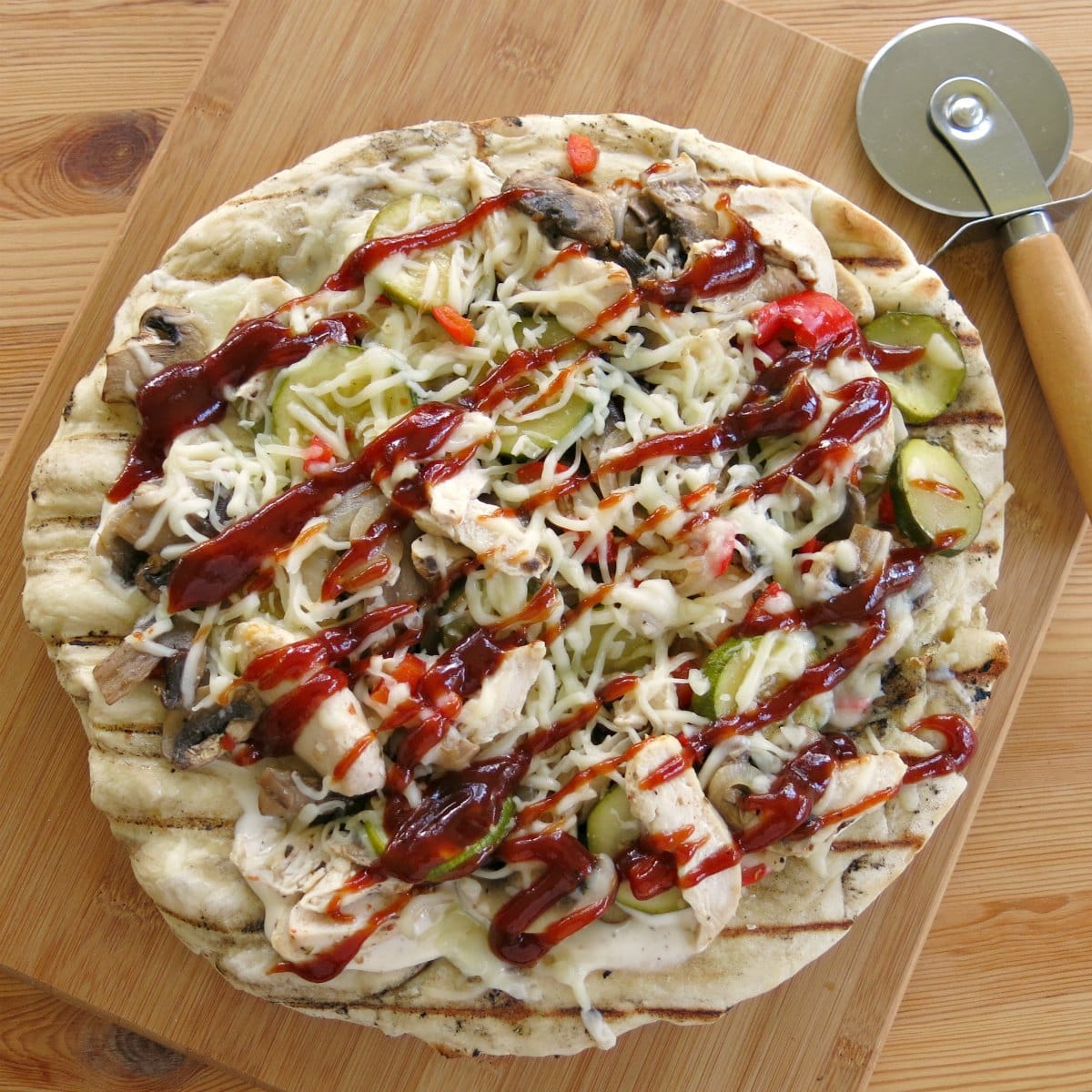 Finished BBQ Chicken Pizza on cutting board with a pizza cutter.