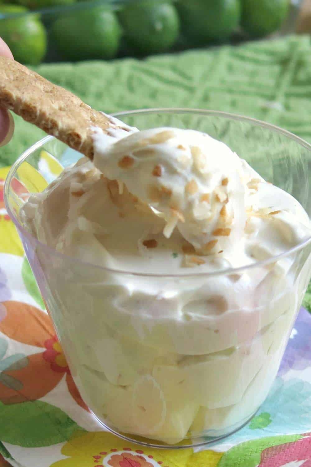 A graham cracker lifting out some Key Lime Pie Dip from a glass.