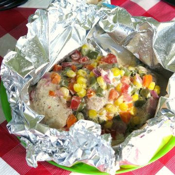 Open ranch chicken foil packets with confetti vegetables on top.