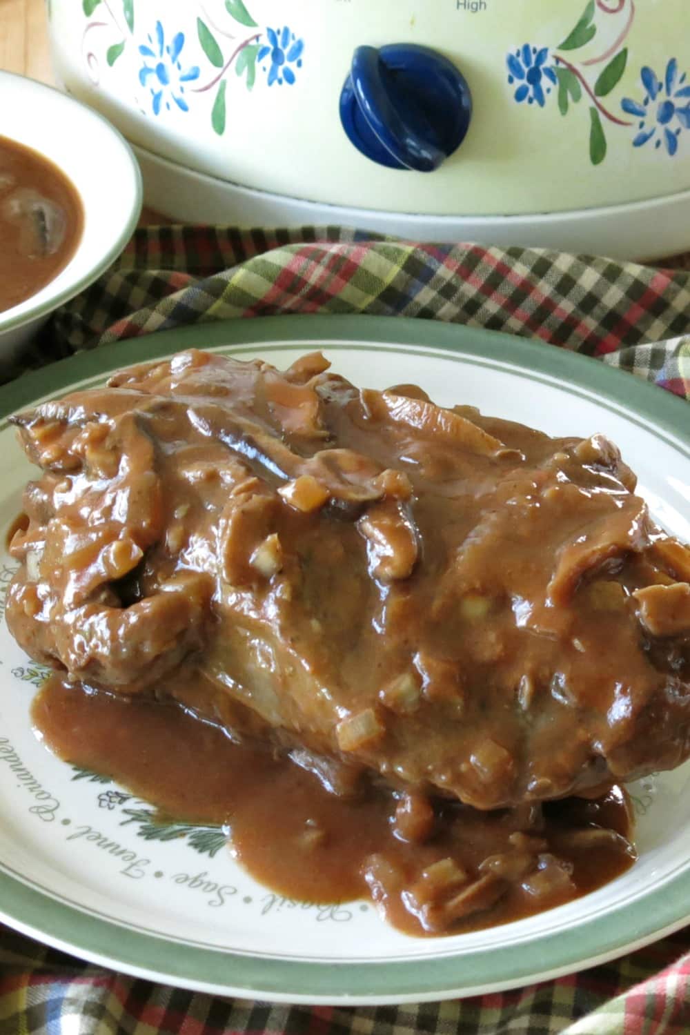 Pot Roast topped with mushroom wine sauce on plate with slow cooker behind it.