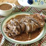 Beef shoulder roast topped with red wine mushroom sauce on a plate.