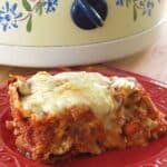 Slice of slow cooker vegetarian lasagna on a plate in front of a slow cooker.