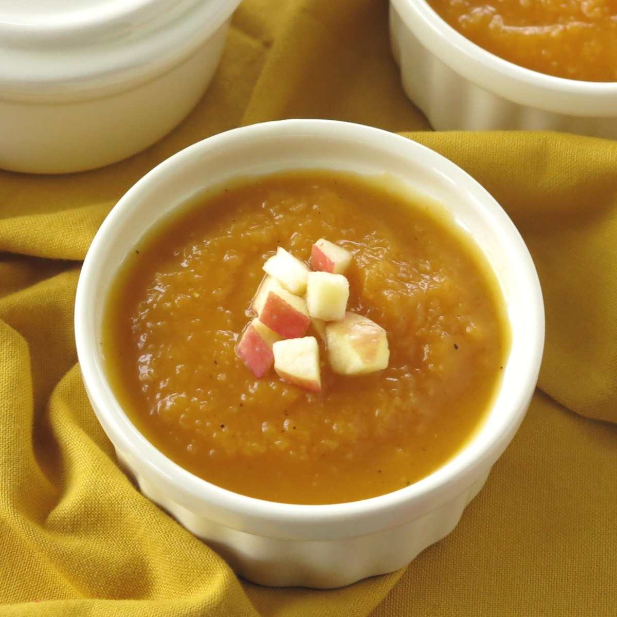 Spicy Butternut squash soup with apple in a cup with diced apple on top.