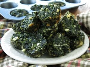 Spinach, feta, egg muffins on a white plate in front of a mini muffin tin.