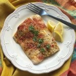 Baked Corvina with lemon crust on plate with fork and lemon wedges.